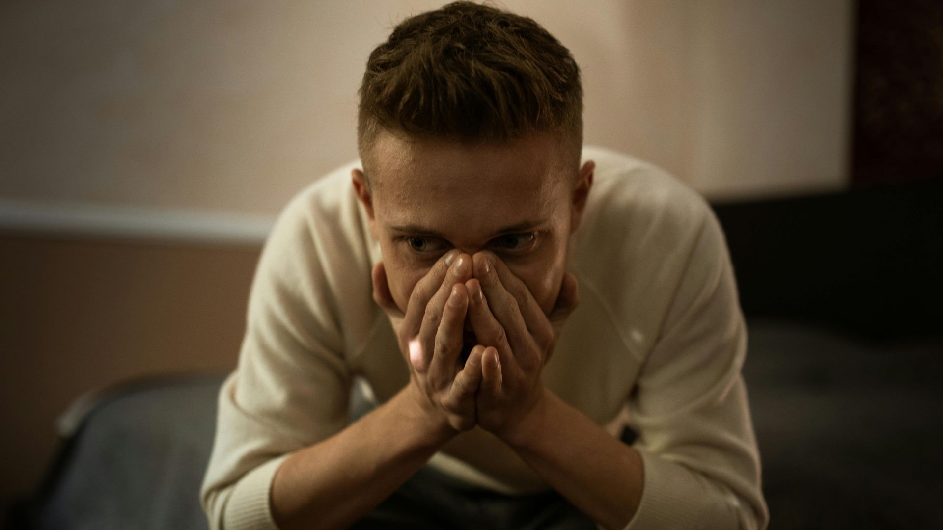A worried man indoors covering his face with hands, depicting stress or contemplation.