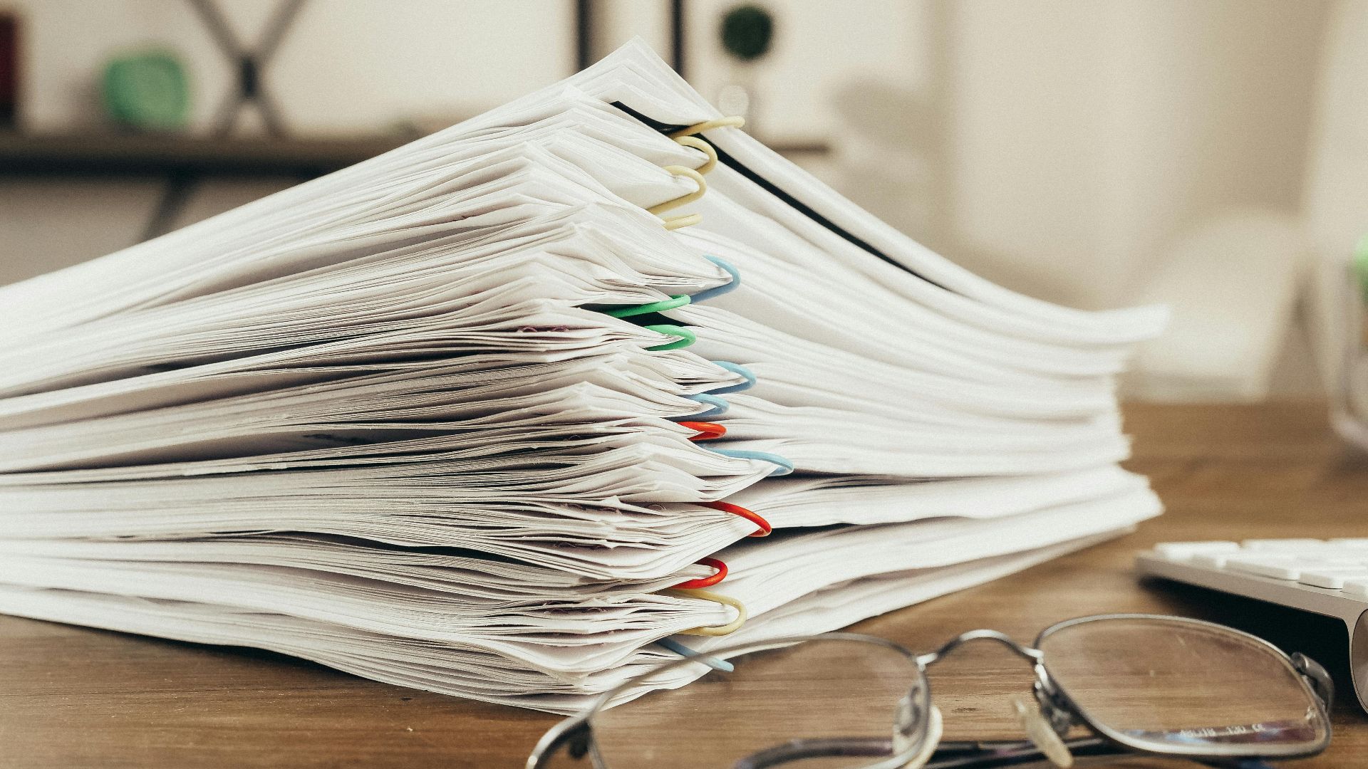Close-up of a stack of office papers on a desk with glasses, emphasizing organization.