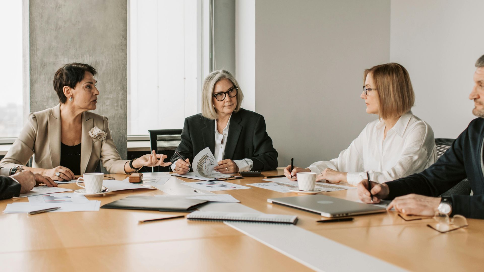 Five business professionals engaged in a meeting in a modern office setting, discussing documents and ideas.