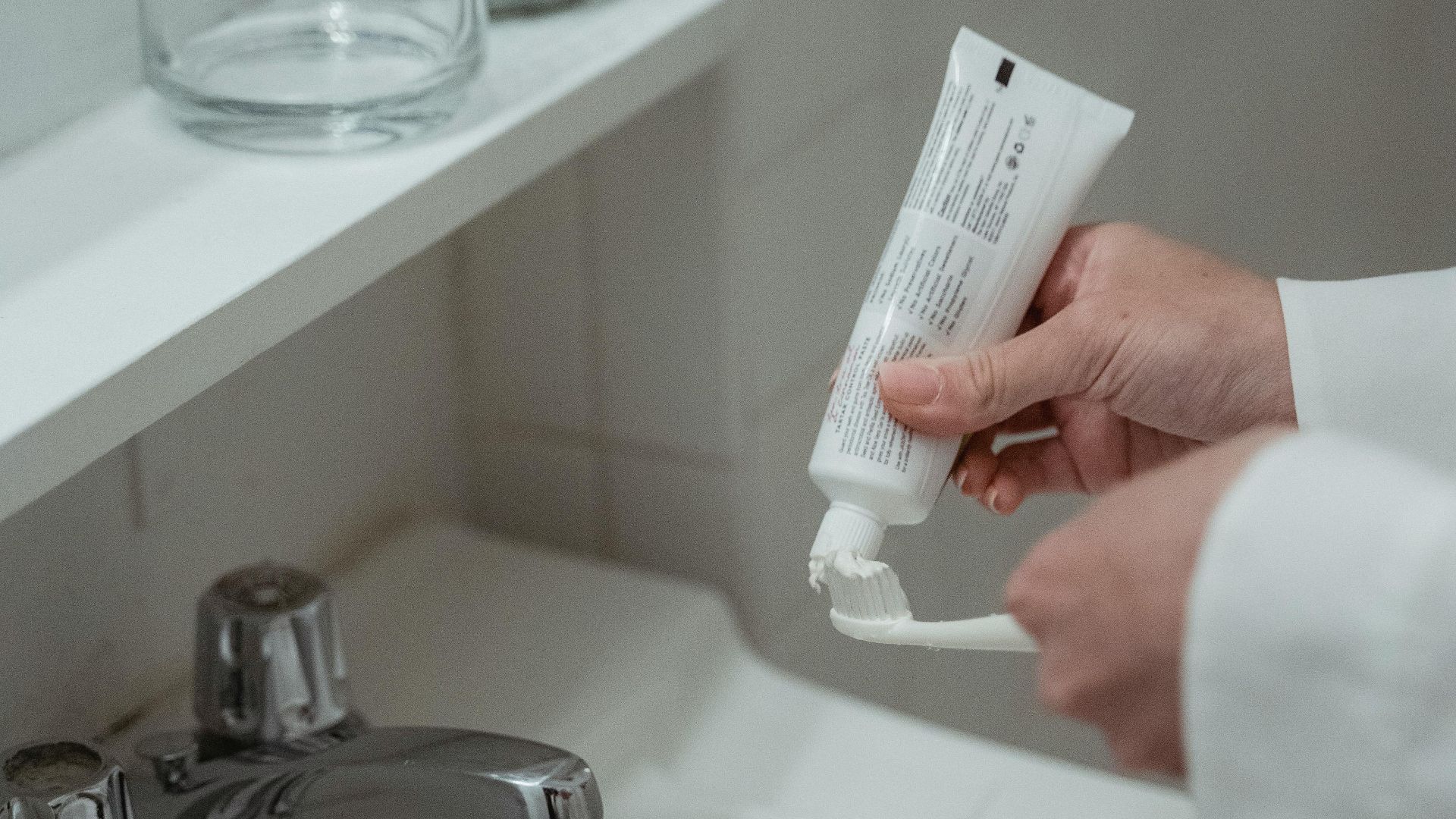 Close-up of a person applying toothpaste on a toothbrush in a clean, modern bathroom setting.