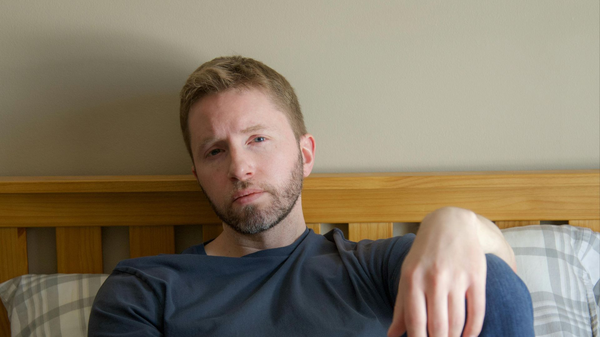 Man with contemplative look relaxing on bed at home, daytime lighting.