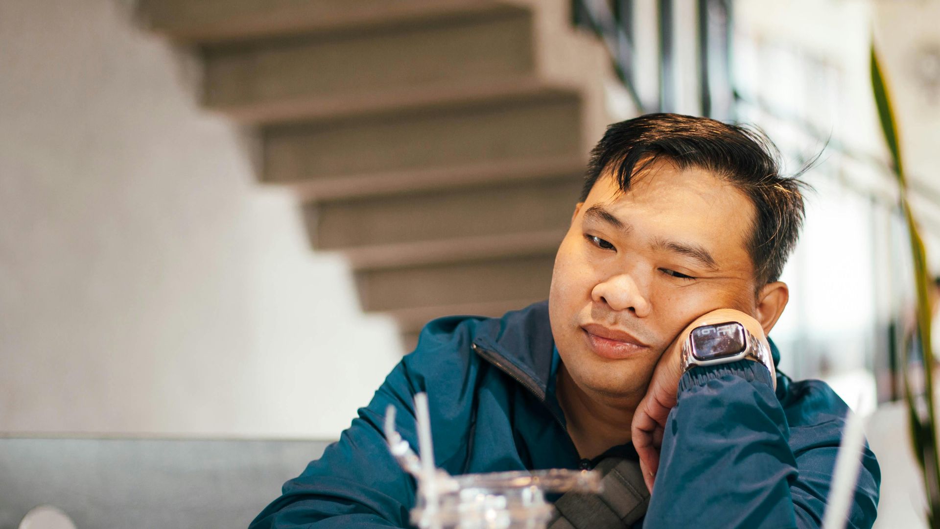Man in casual wear sitting thoughtfully in a modern café, empty drink glasses on table.