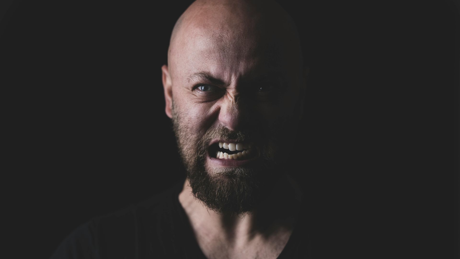 Close-up of a bald and bearded man showing a fierce expression in a dark setting.