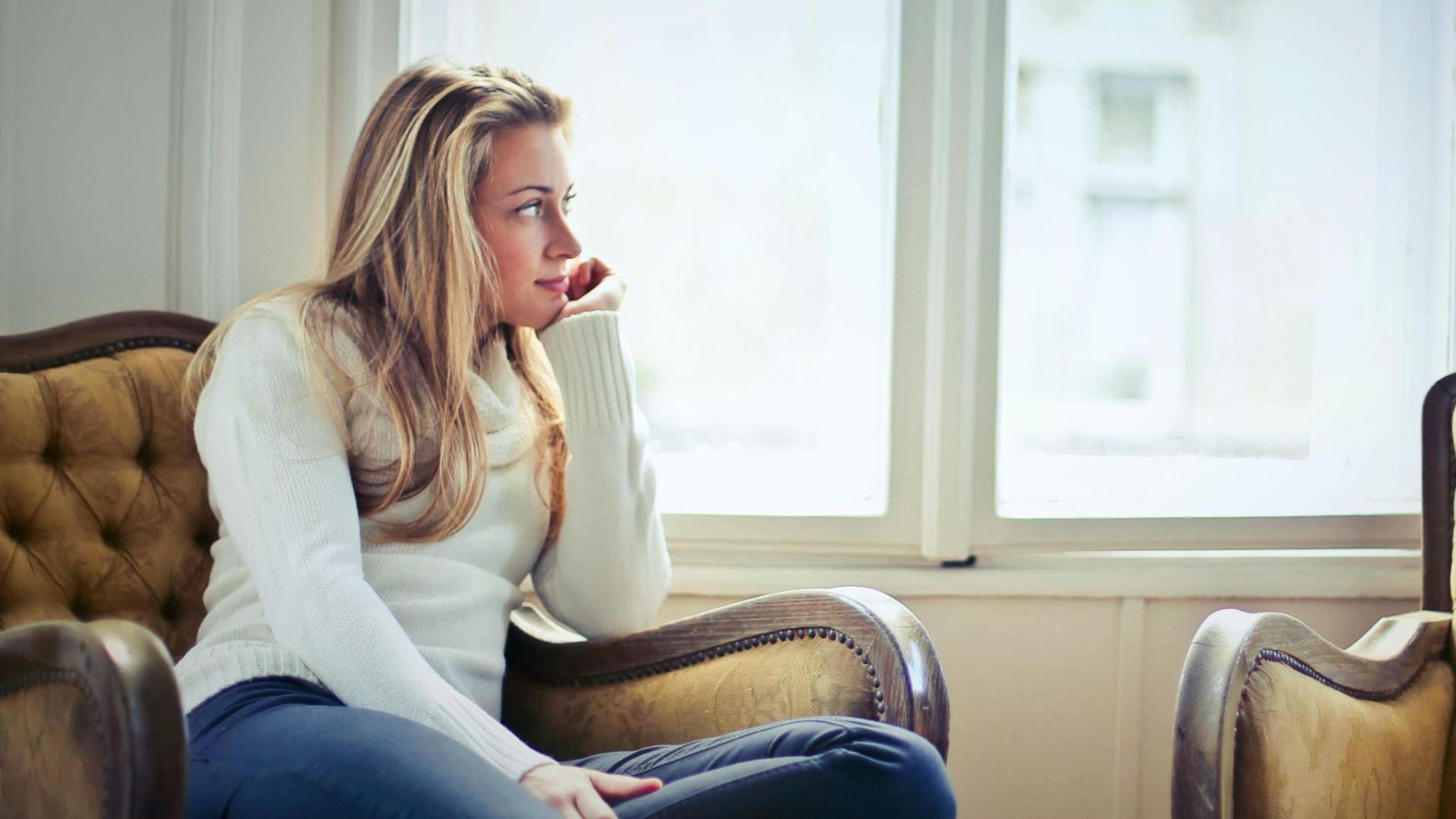 Young woman in a cozy armchair by a window, enjoying peaceful relaxation at home.