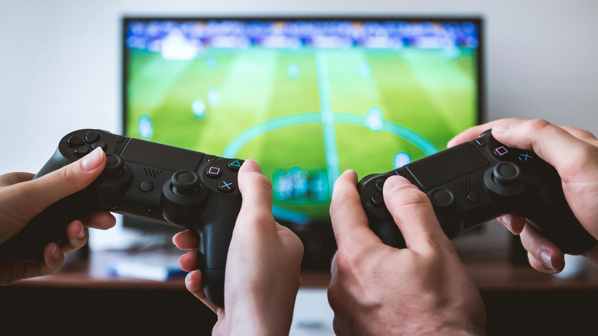 Close-up of hands holding gaming controllers in front of a TV. Engaged in a video gaming session.