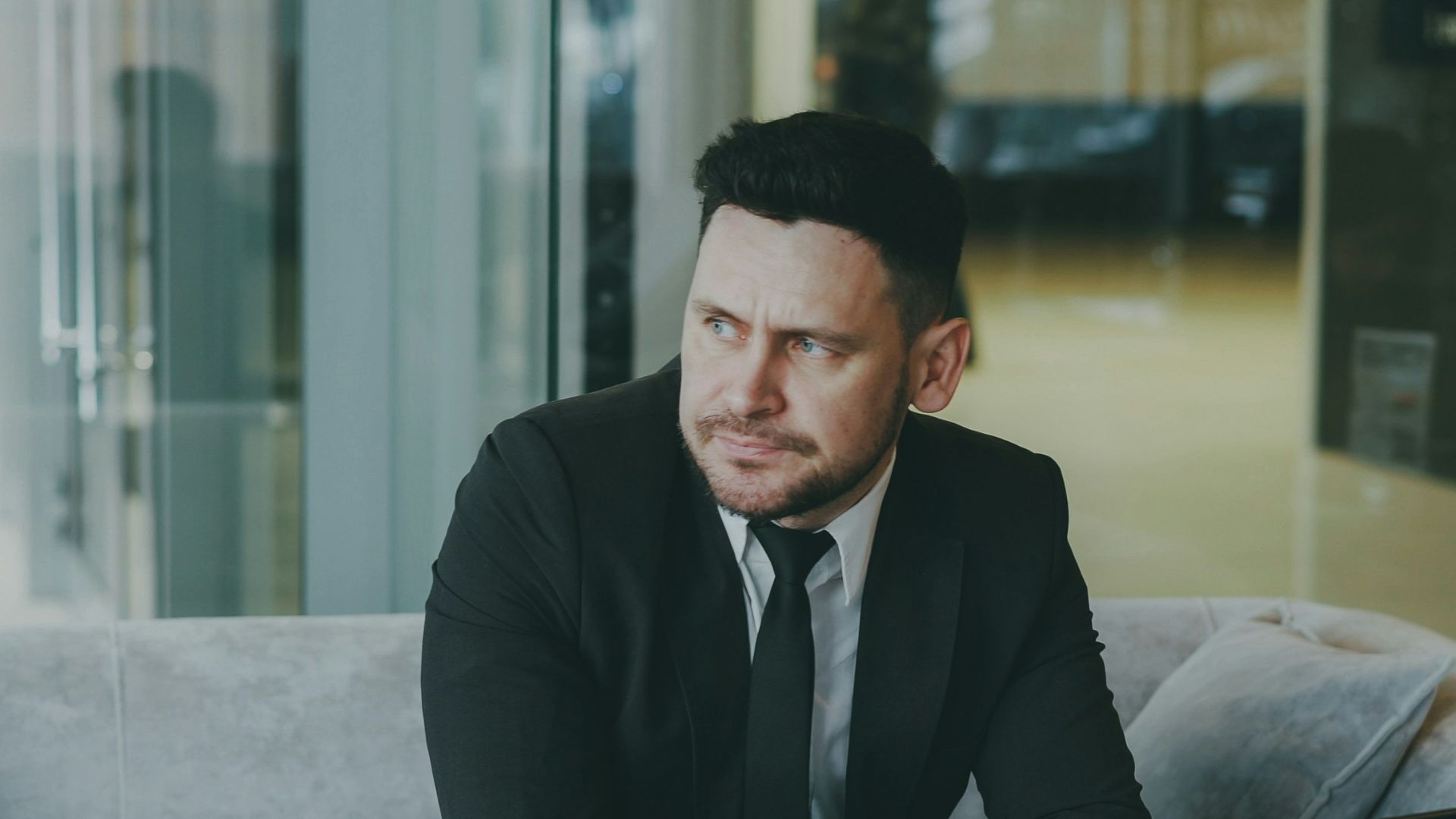 Man in suit sitting at table with laptop and coffee.