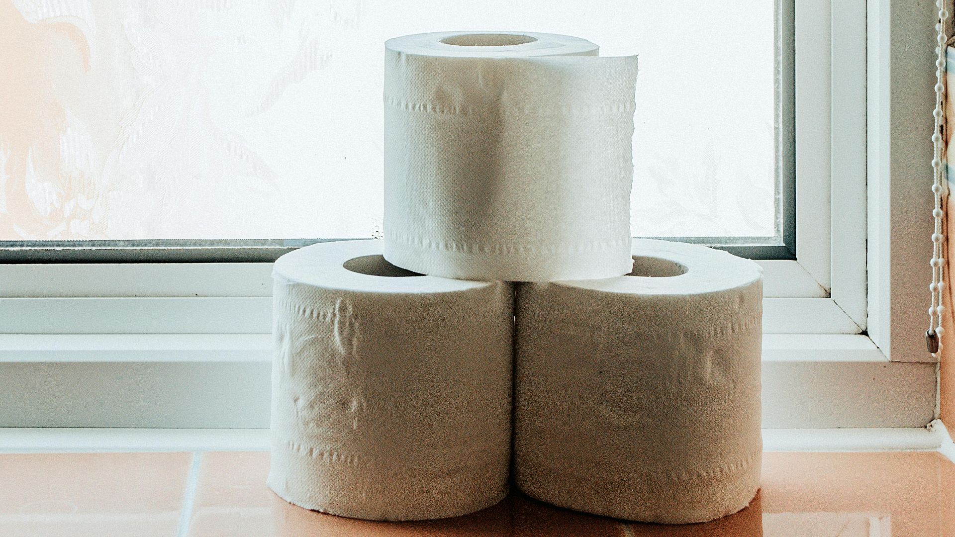 Three toilet paper rolls neatly stacked on a windowsill in a well-lit bathroom.