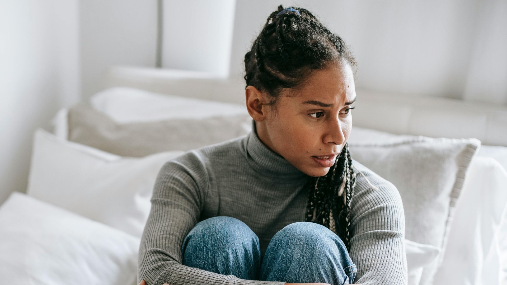 Frustrated distressed ethnic female thinking on problem while sitting on bed and looking away