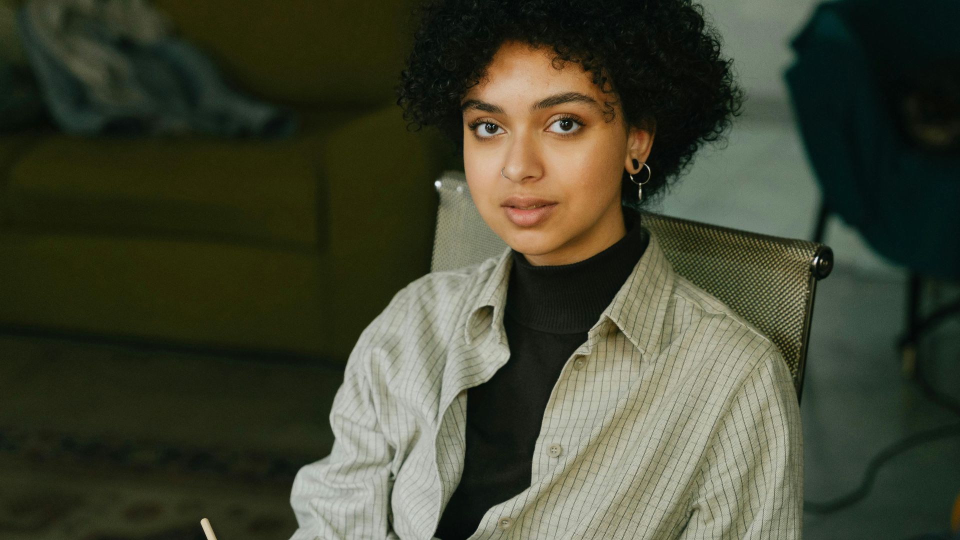 A young woman with curly hair pens notes in a notebook while sitting indoors.