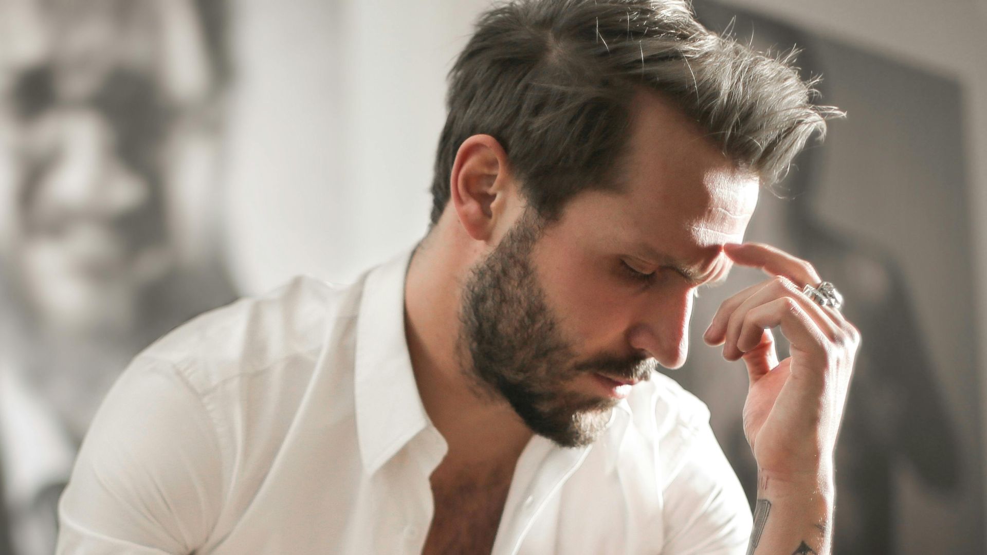 Low angle of handsome bearded man in white shirt touching forehead in deep thoughts sitting at piano