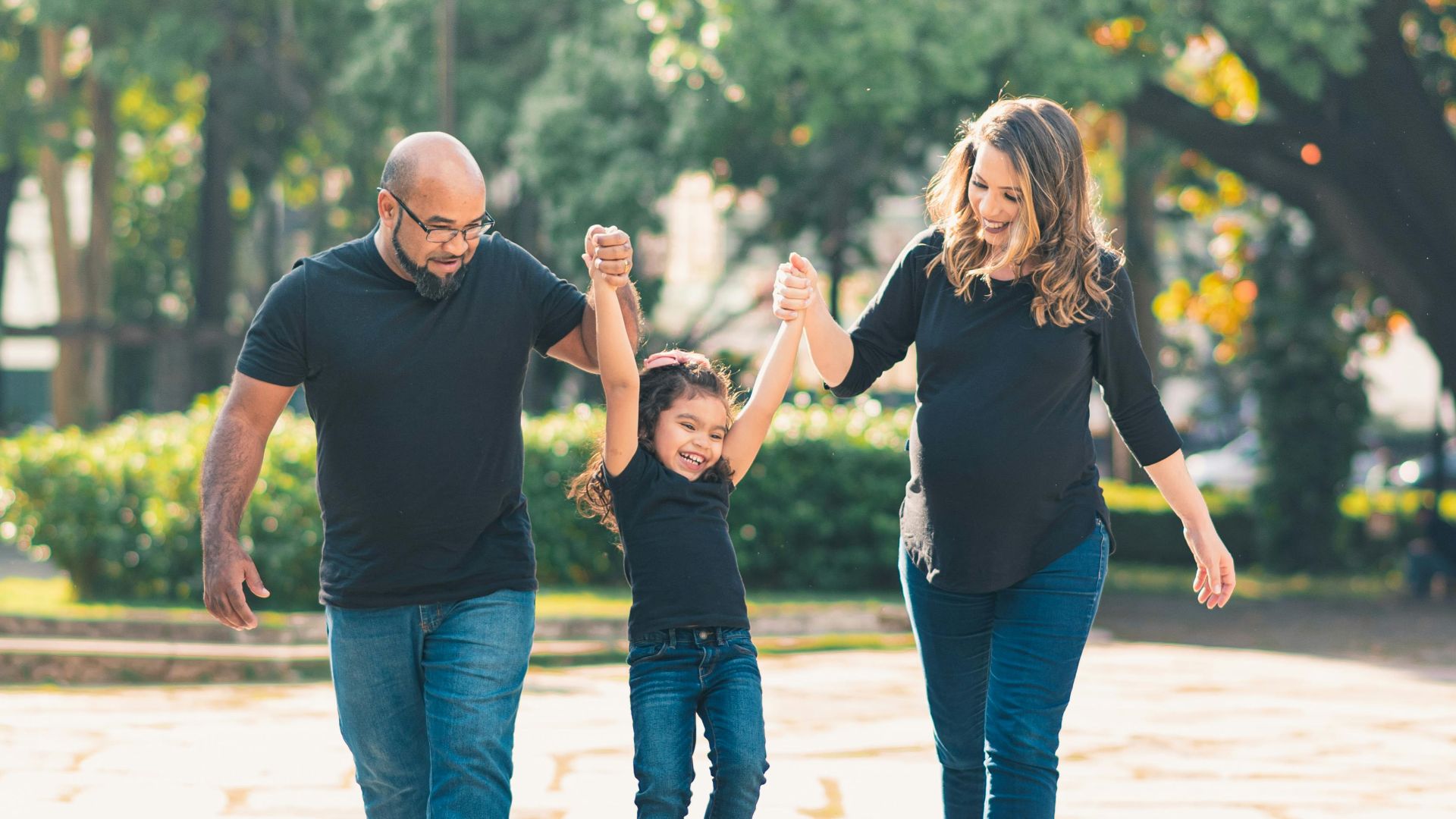 Joyful family enjoying a sunny walk in the park, lifting their daughter with smiles.
