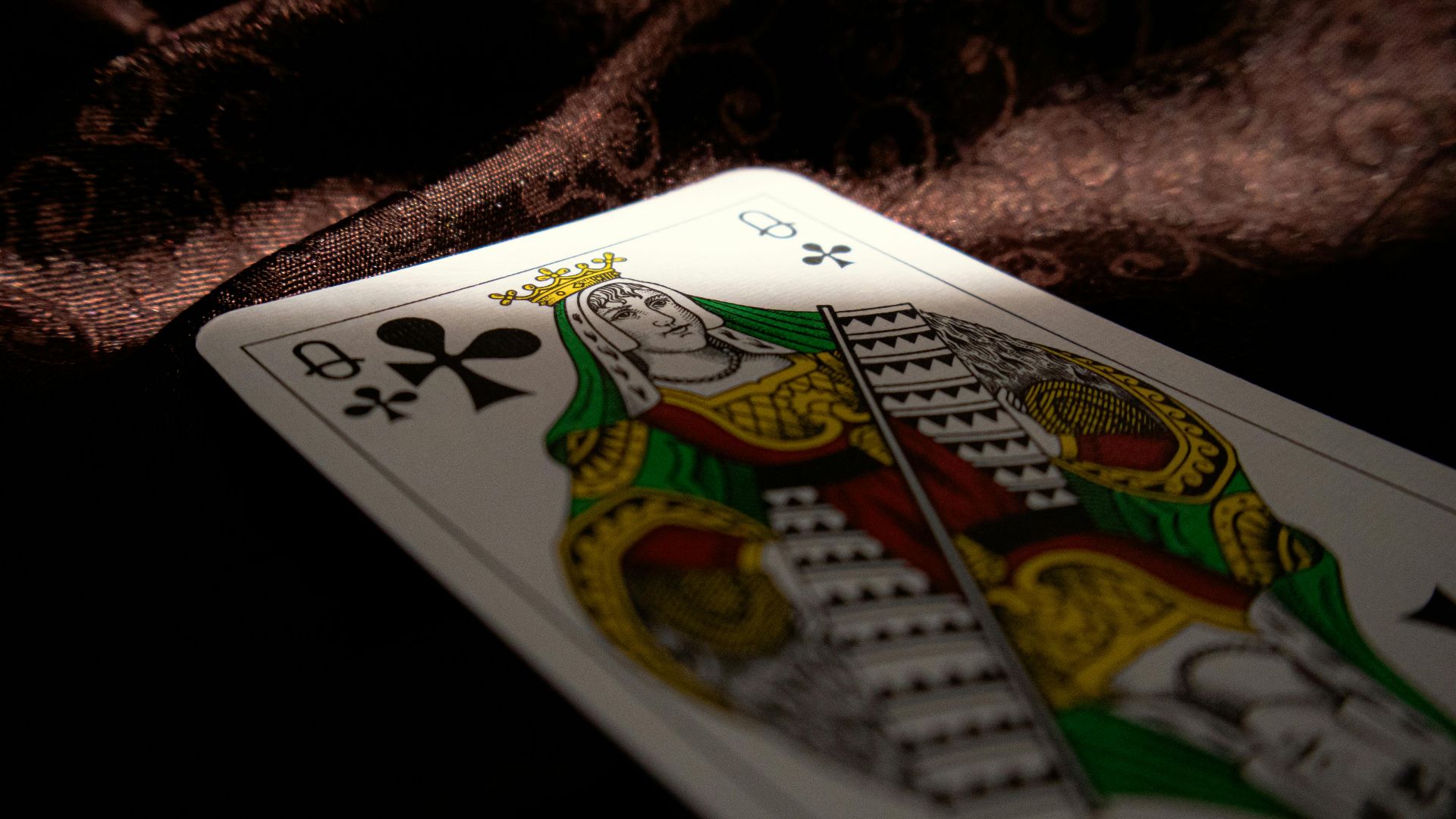 Close-up of a Queen of Clubs playing card on a dark velvet fabric, highlighting themes of gambling and chance.
