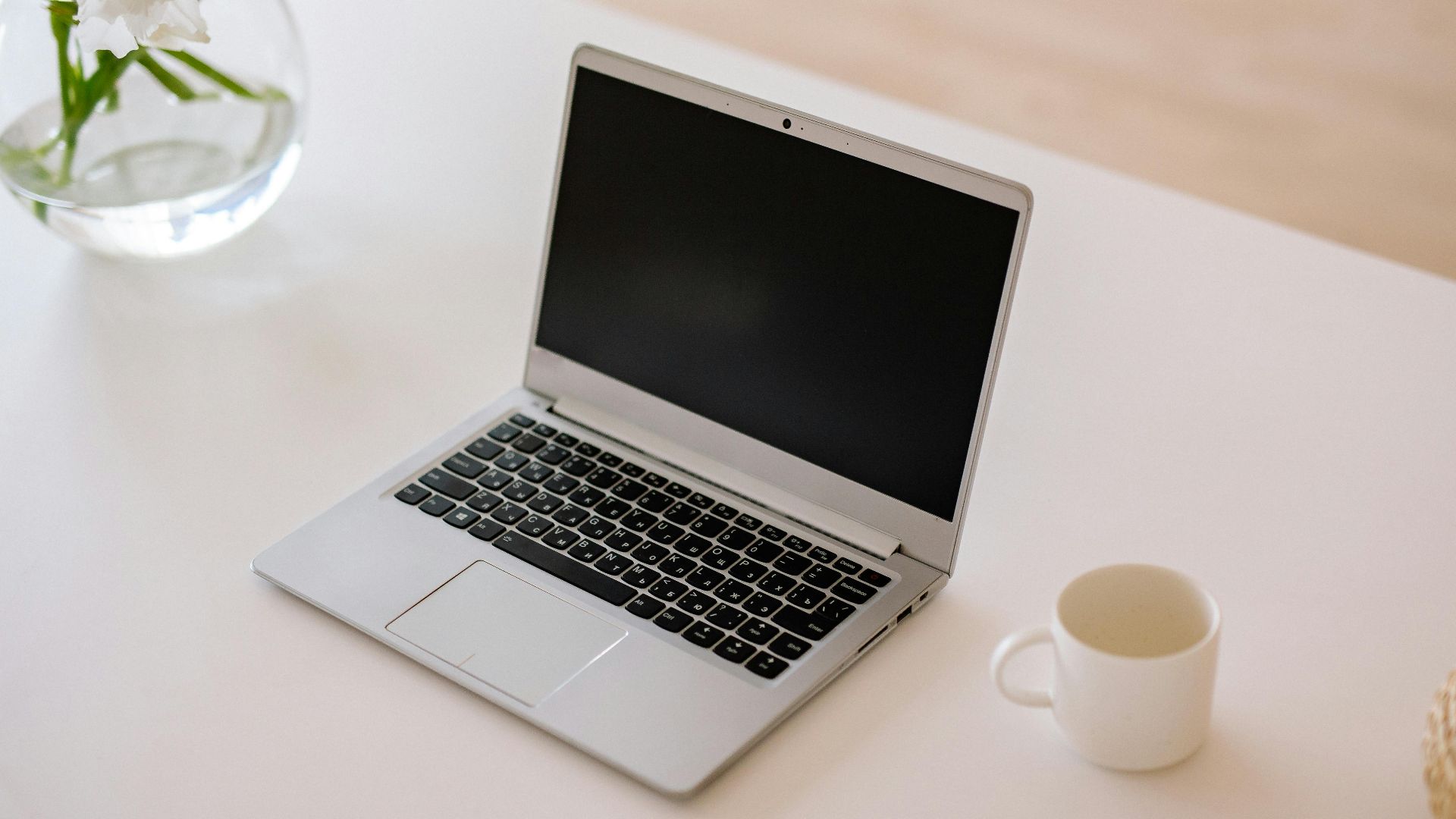 A minimalist workspace with an open laptop, coffee mug, and vase on a bright indoor table.