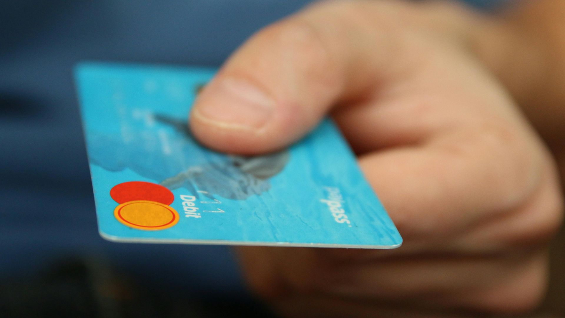 A close-up shot of a hand offering a blue debit card for payment.