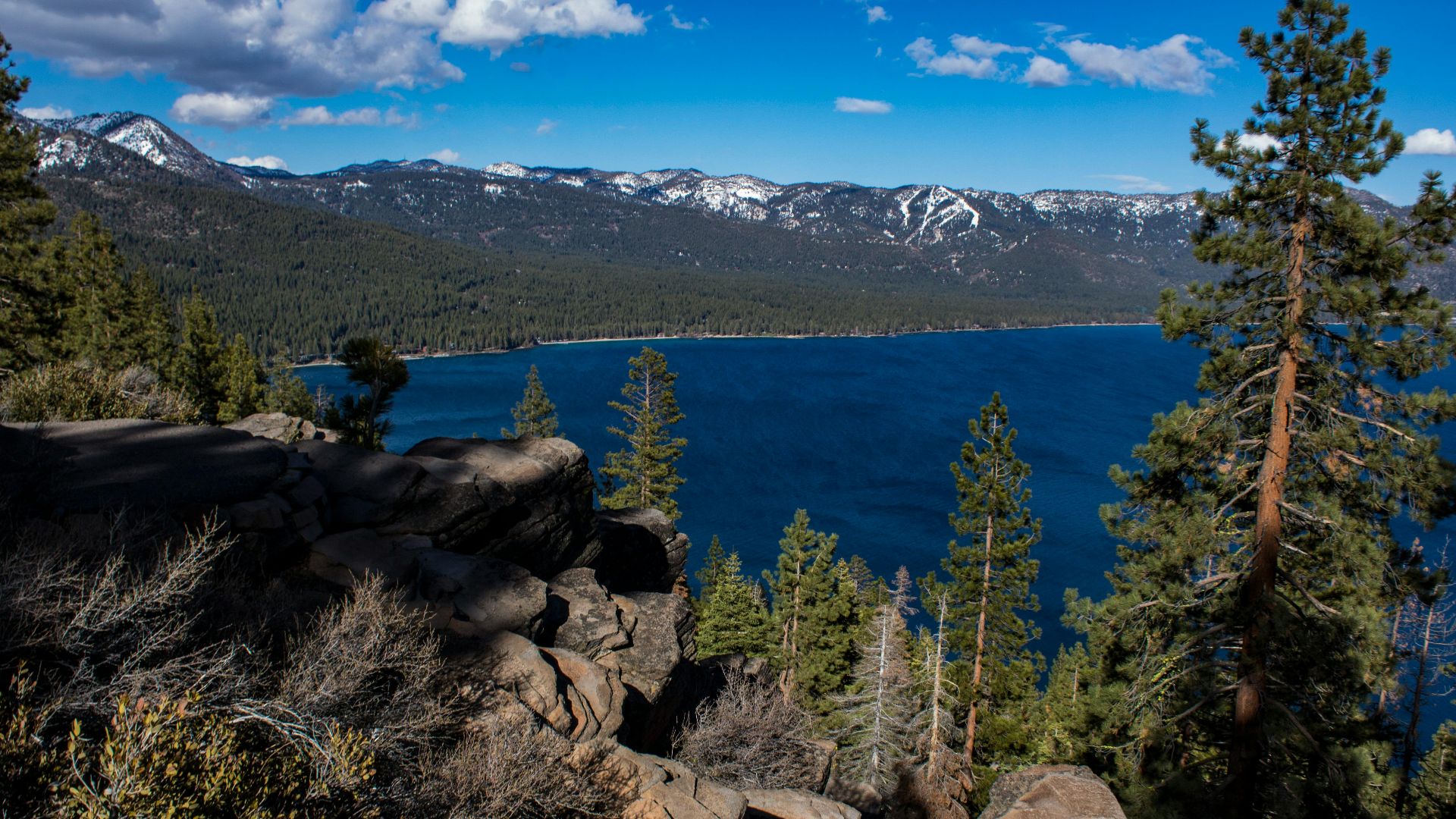Breathtaking view of Lake Tahoe with surrounding forests and mountains, captured from a rocky cliff.