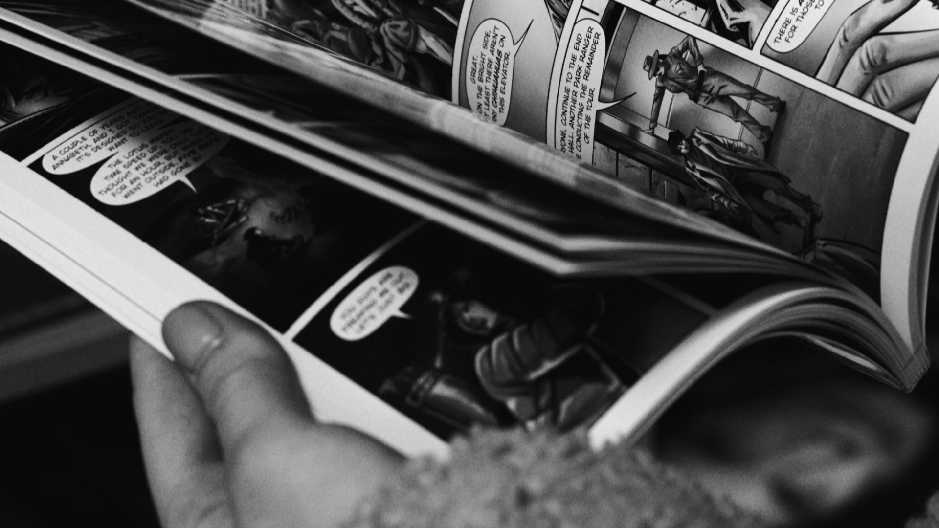 Close-up of hands reading a black and white comic book, focus on the comic panels.