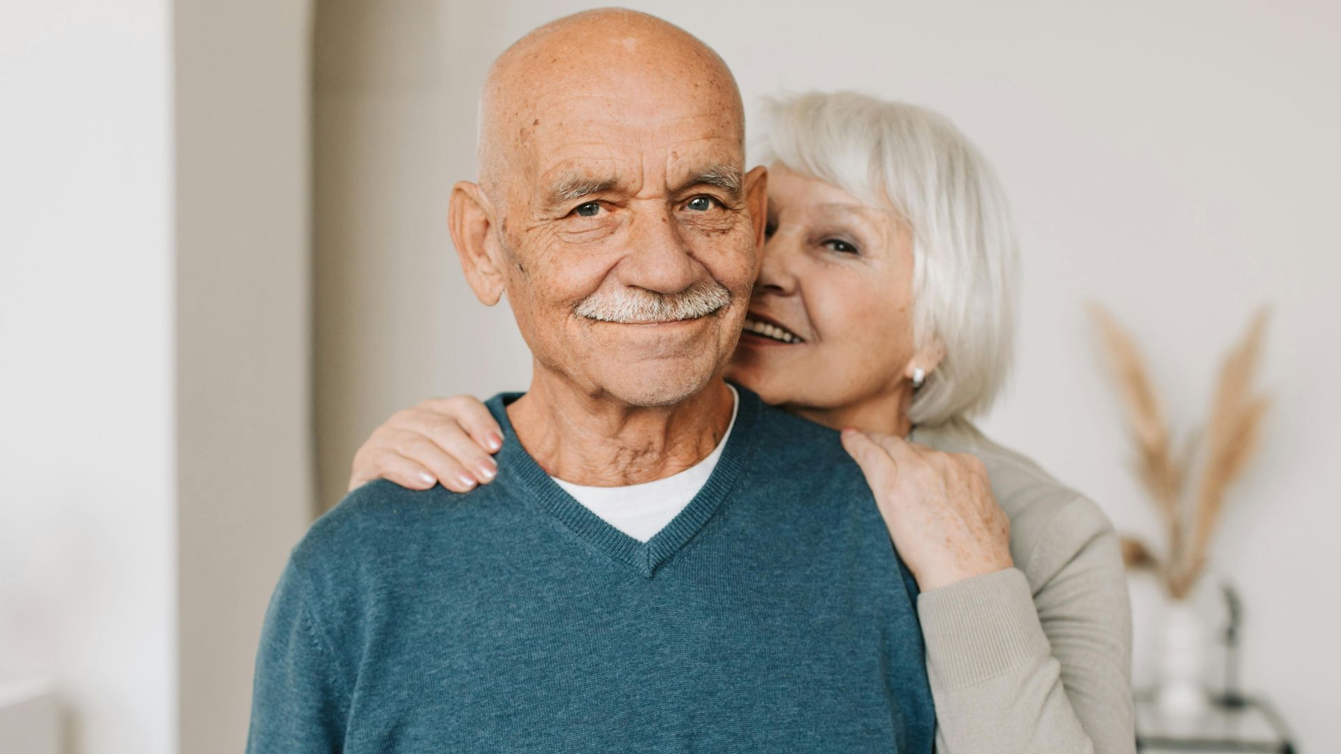 A joyful elderly couple embracing each other in a cozy indoor setting, exuding love and happiness.