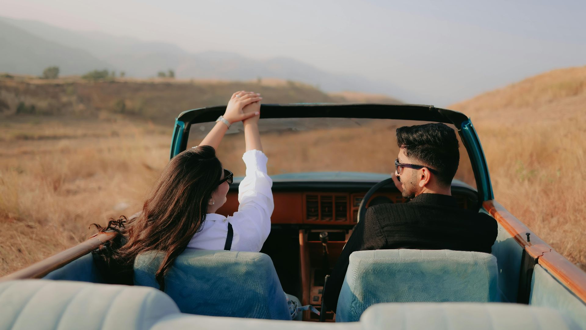 Couple enjoying a scenic drive in a vintage convertible through dry countryside landscape.