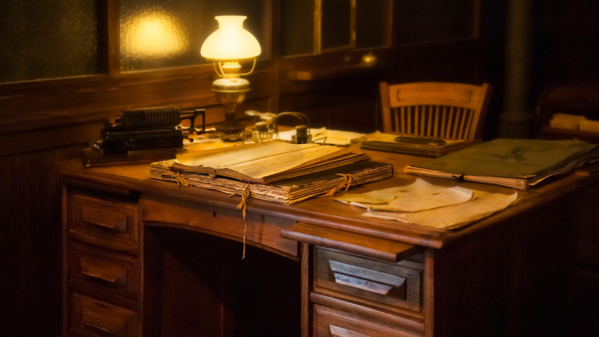 Cozy vintage office setting with an antique typewriter, lamp, and paperwork on a wooden desk.