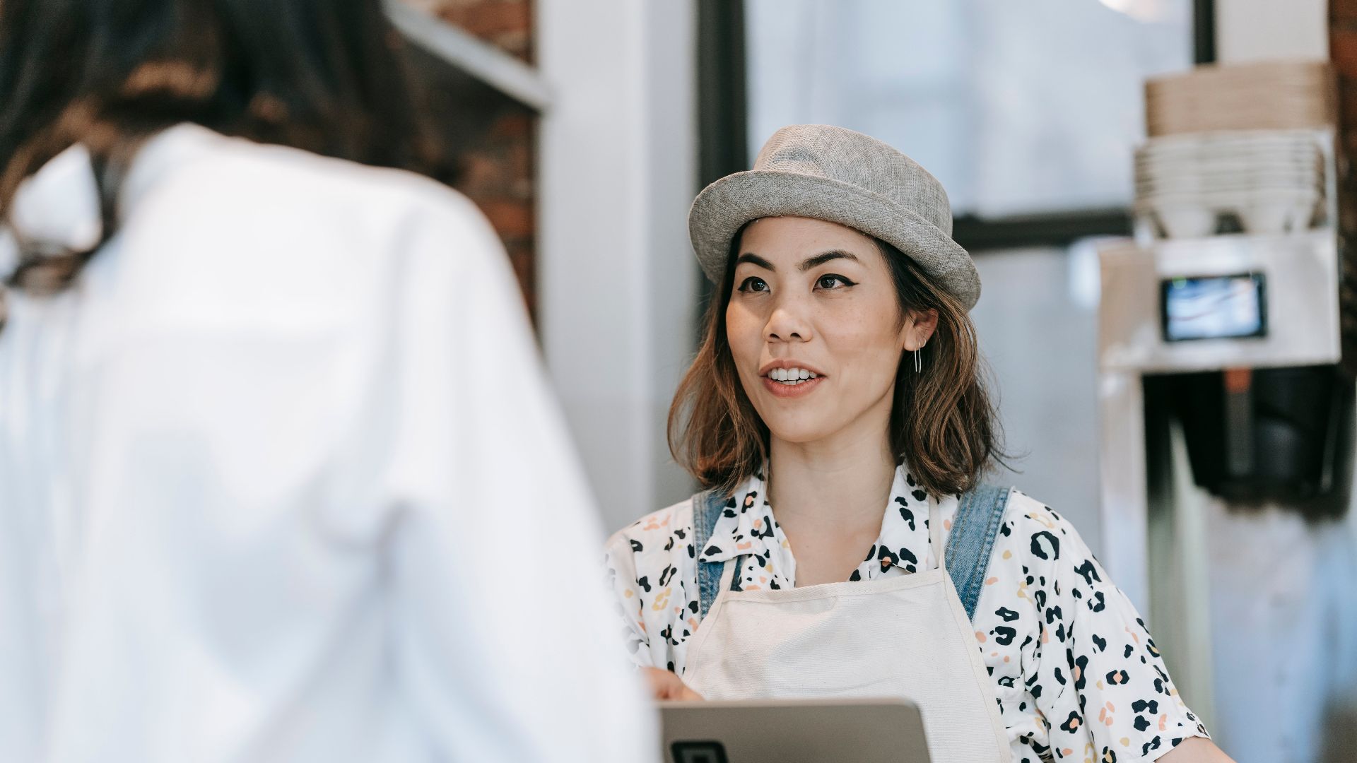 A cheerful barista in a hat takes an order from a customer at a cozy coffee shop counter.