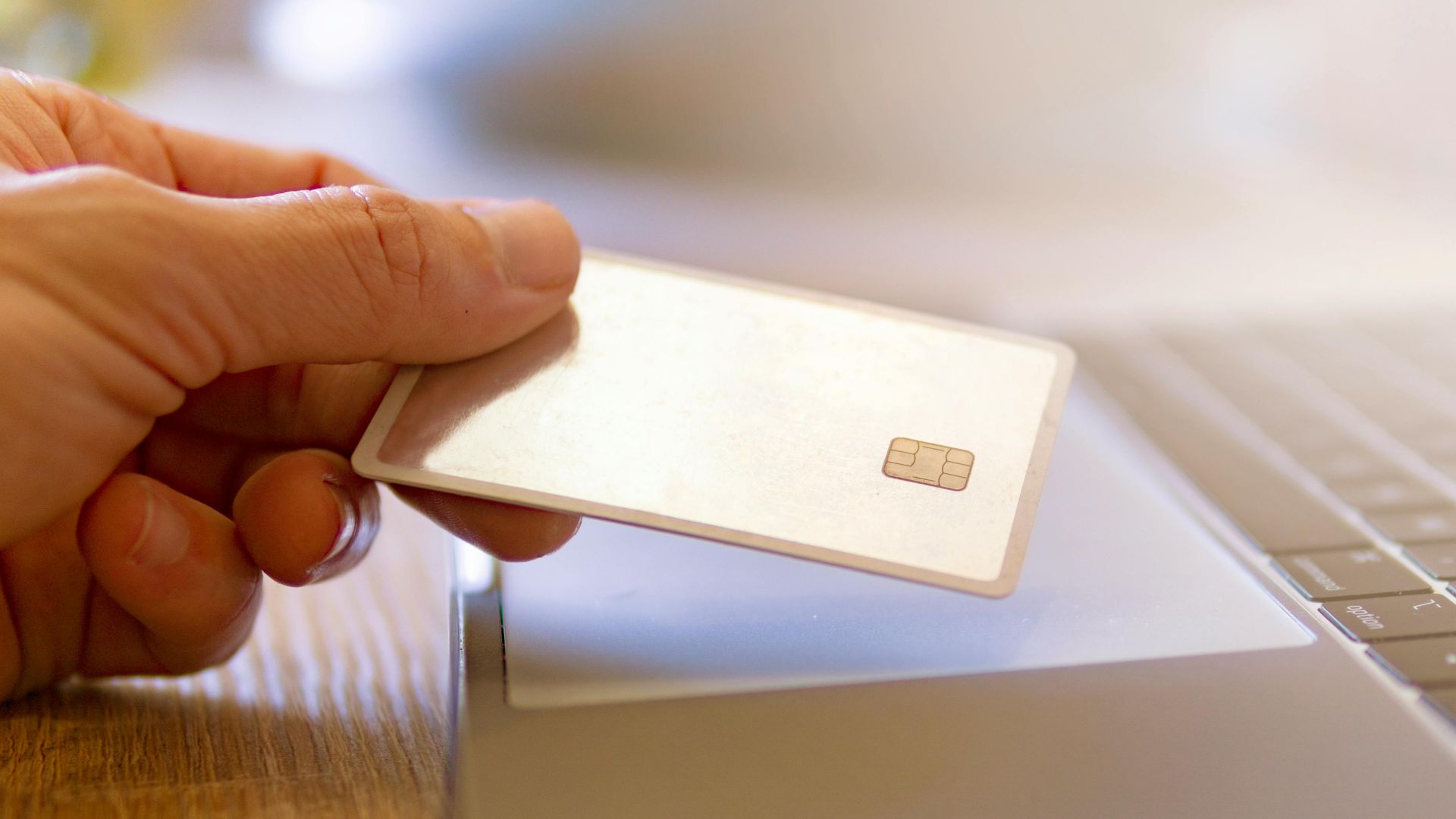 A person holds a credit card near a laptop for online shopping.