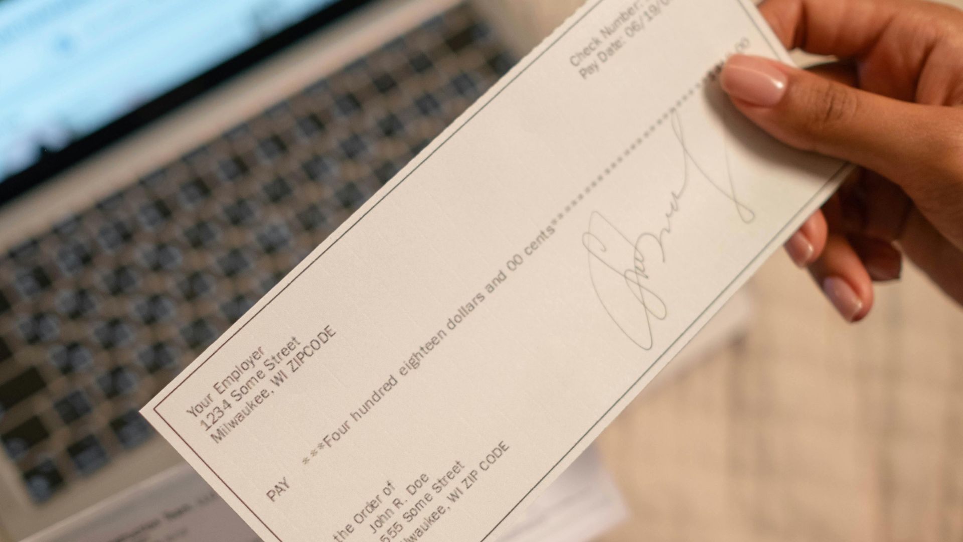 Individual holding a cheque over laptop, signifying online banking or financial transaction.