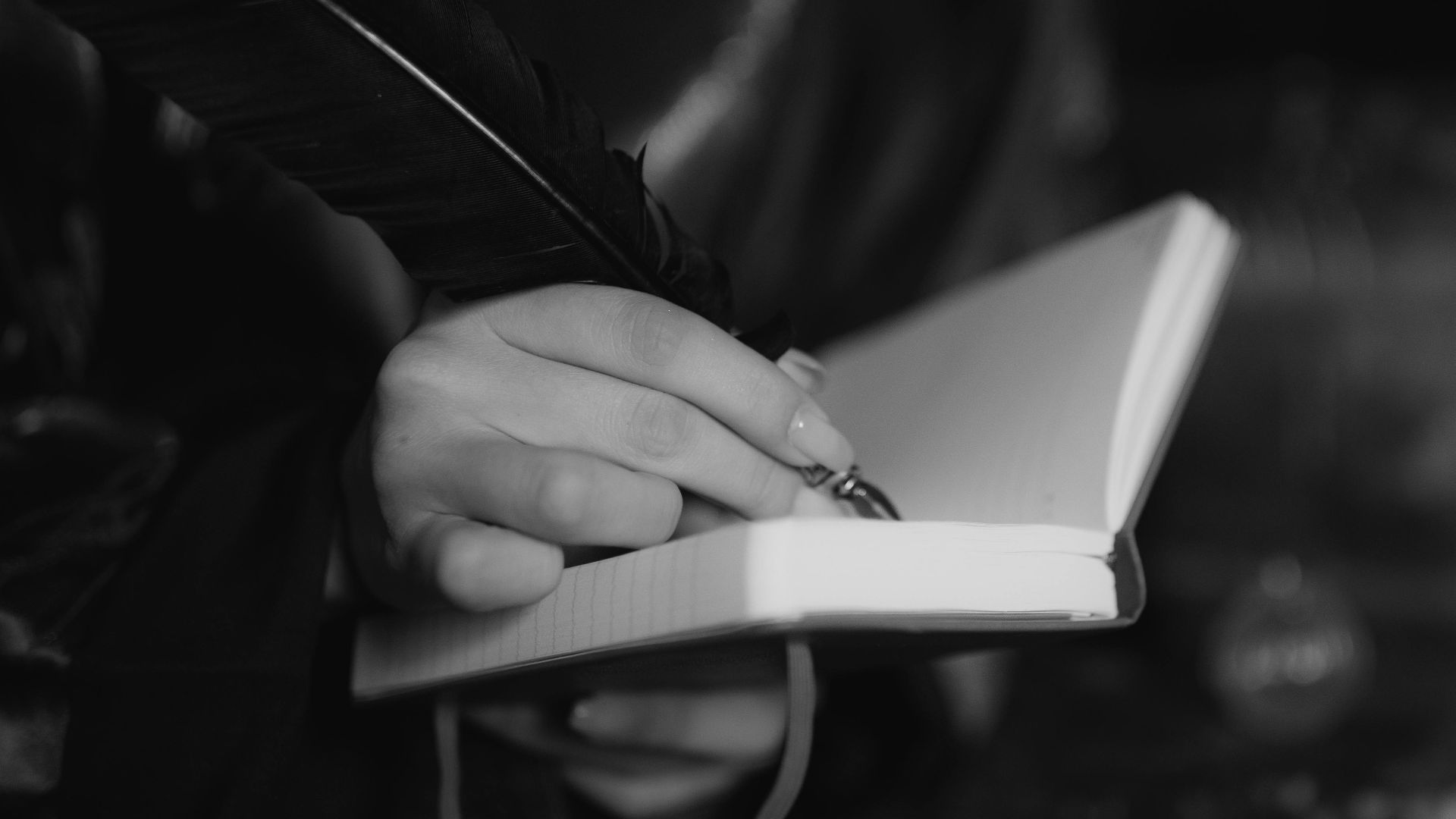A hand writing in a notebook with a quill pen, captured in black and white for a classic feel.