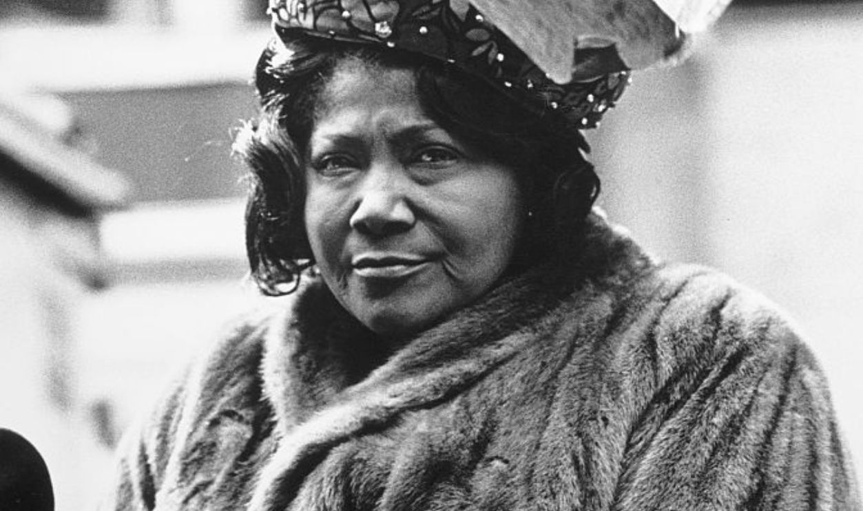 American gospel singer Mahalia Jackson, wearing a fur coat, beneath a striped flag (possibly an American flag), United States, circa 1968.