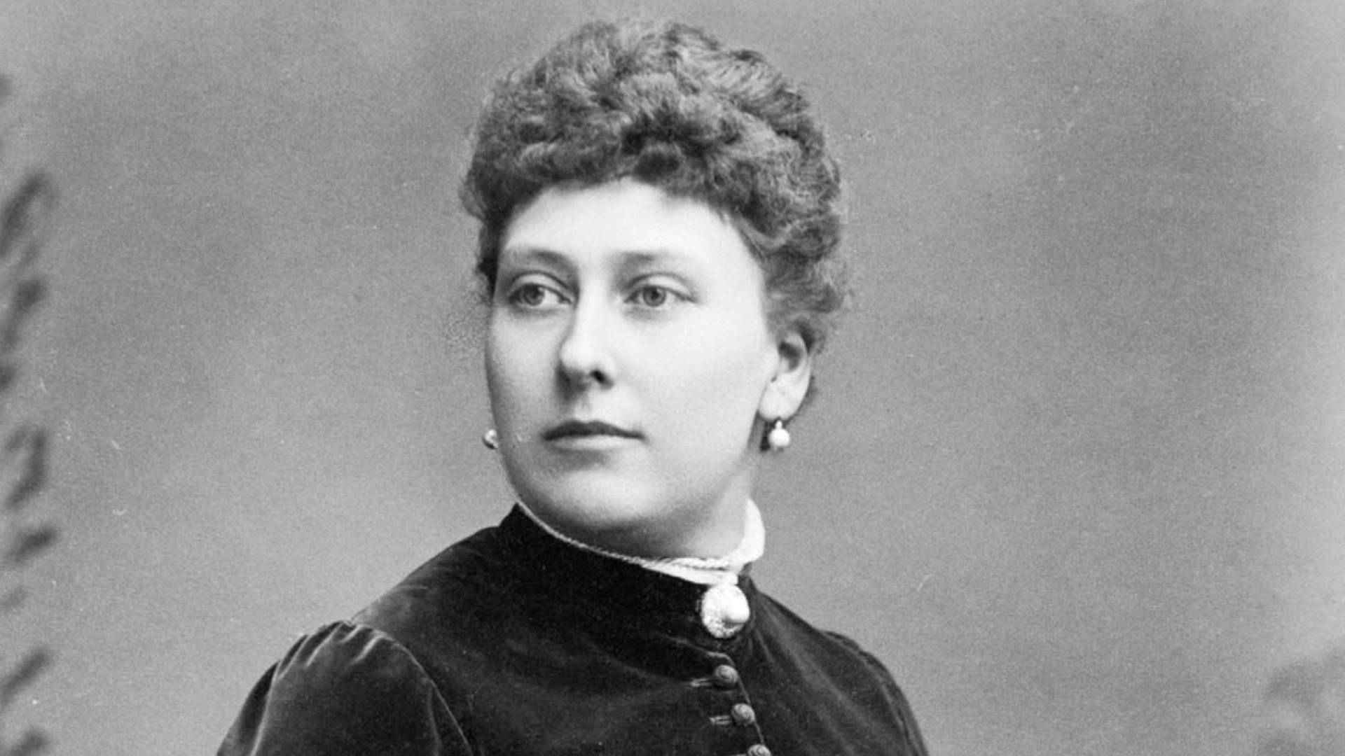 Princess Beatrice seated, holding a piece of ivy or similar on her lap with her right hand. Long-sleeved dress with buttons from neck to waist.