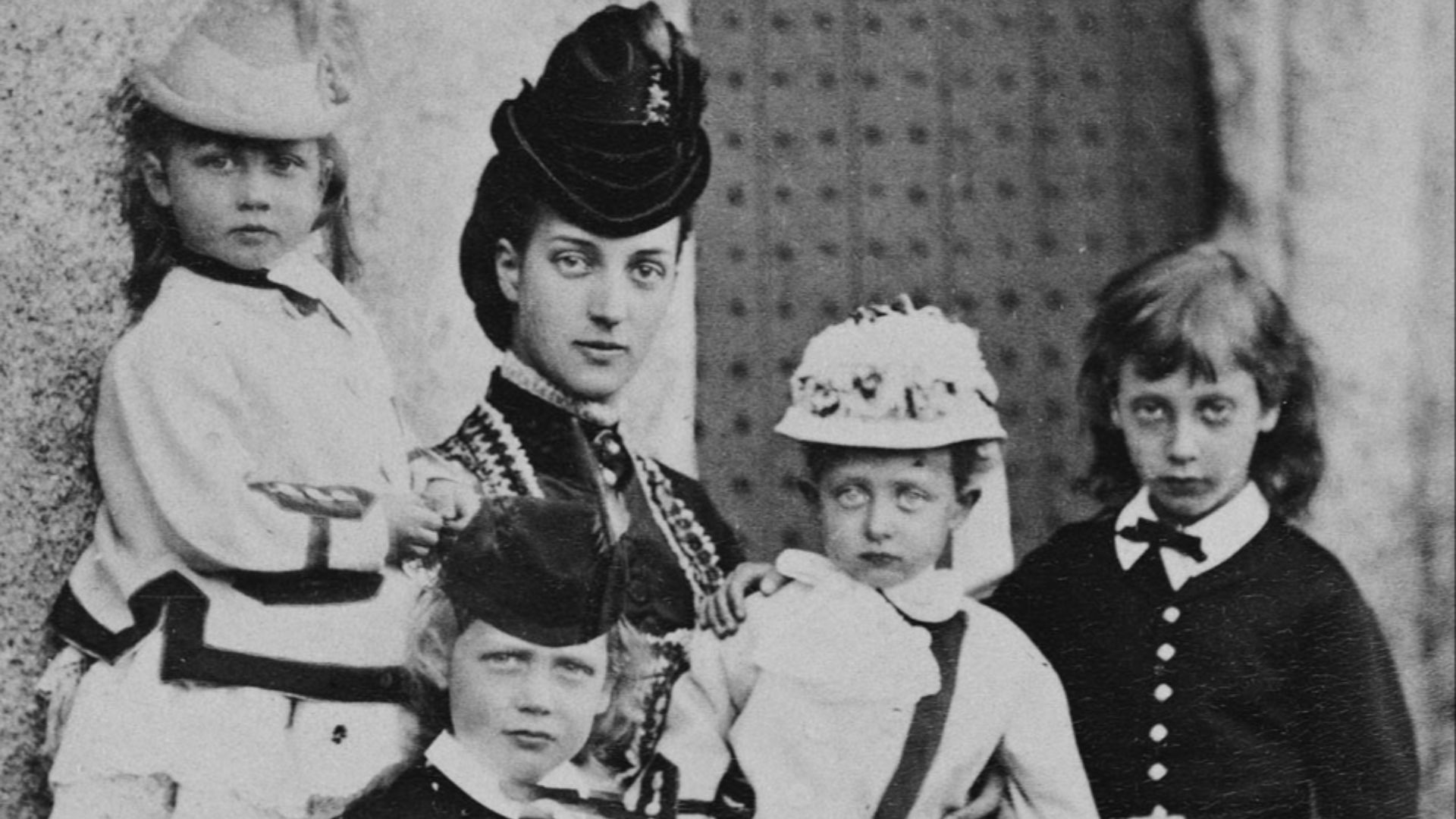 Alexandra, Princess of Wales, seated outside doorway with her 4 eldest children, Abergeldie 1870. Left to r.: Princess Louise; Prince George, his arm round dog; Princess Alexandra; Princess Victoria, on her mother's lap; Prince Albert Victor. Both boys in Highland dress