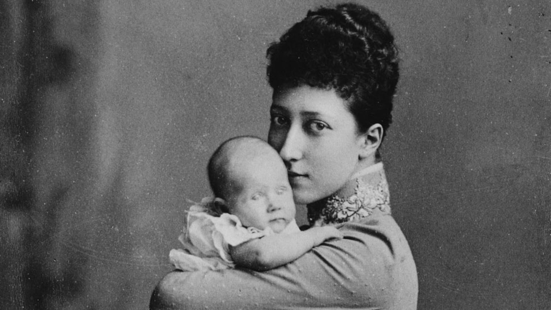 Princess Louise, wearing long-sleeved dress, stands holding her baby daughter