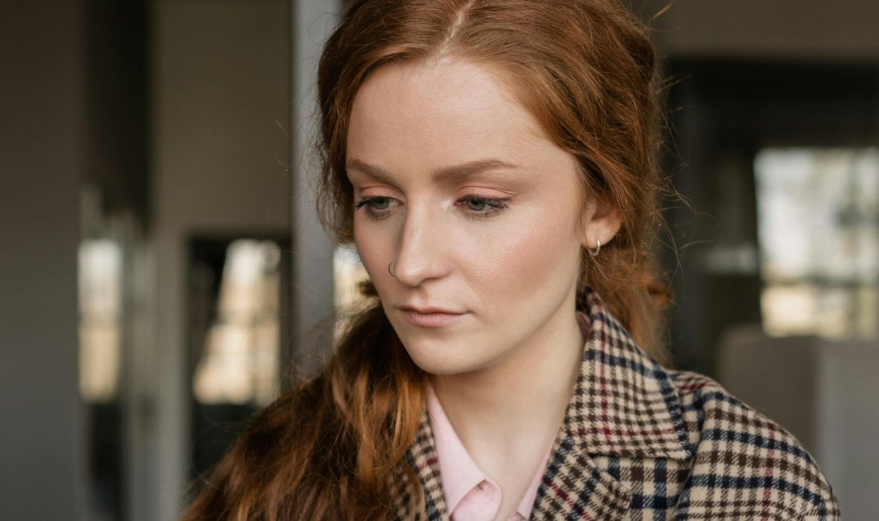 Caucasian woman with a checkered coat intently working on a laptop in an office setting. Professional and modern