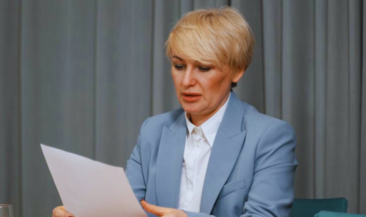Businesswoman in a blazer reviewing documents at a desk. Professional office setting with laptop and papers