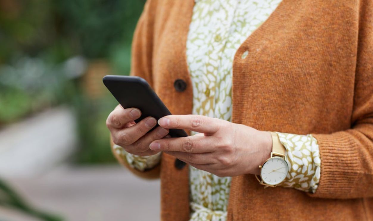 Elderly person's hands holding a smartphone in a casual setting, wearing a watch.