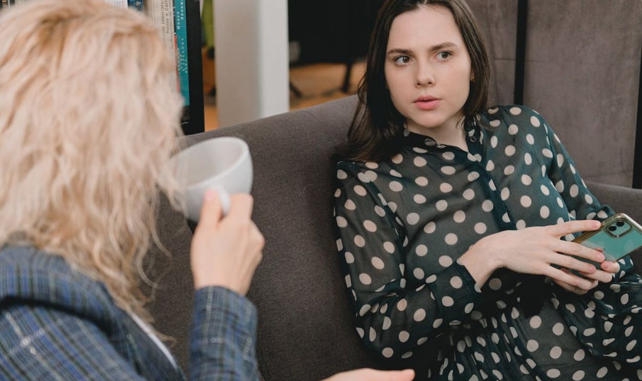 Two adult women having a conversation over coffee on a cozy couch indoors