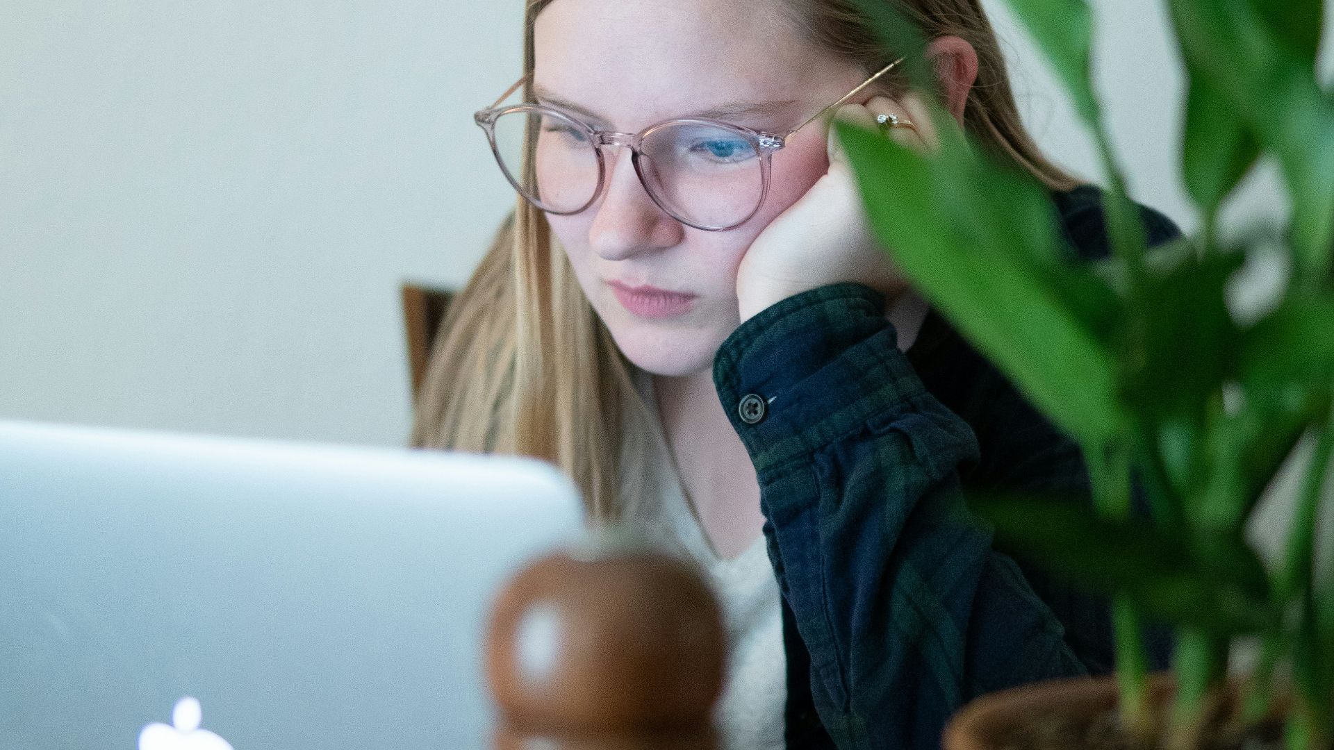 woman in blue denim jacket wearing eyeglasses sitting beside table with macbook