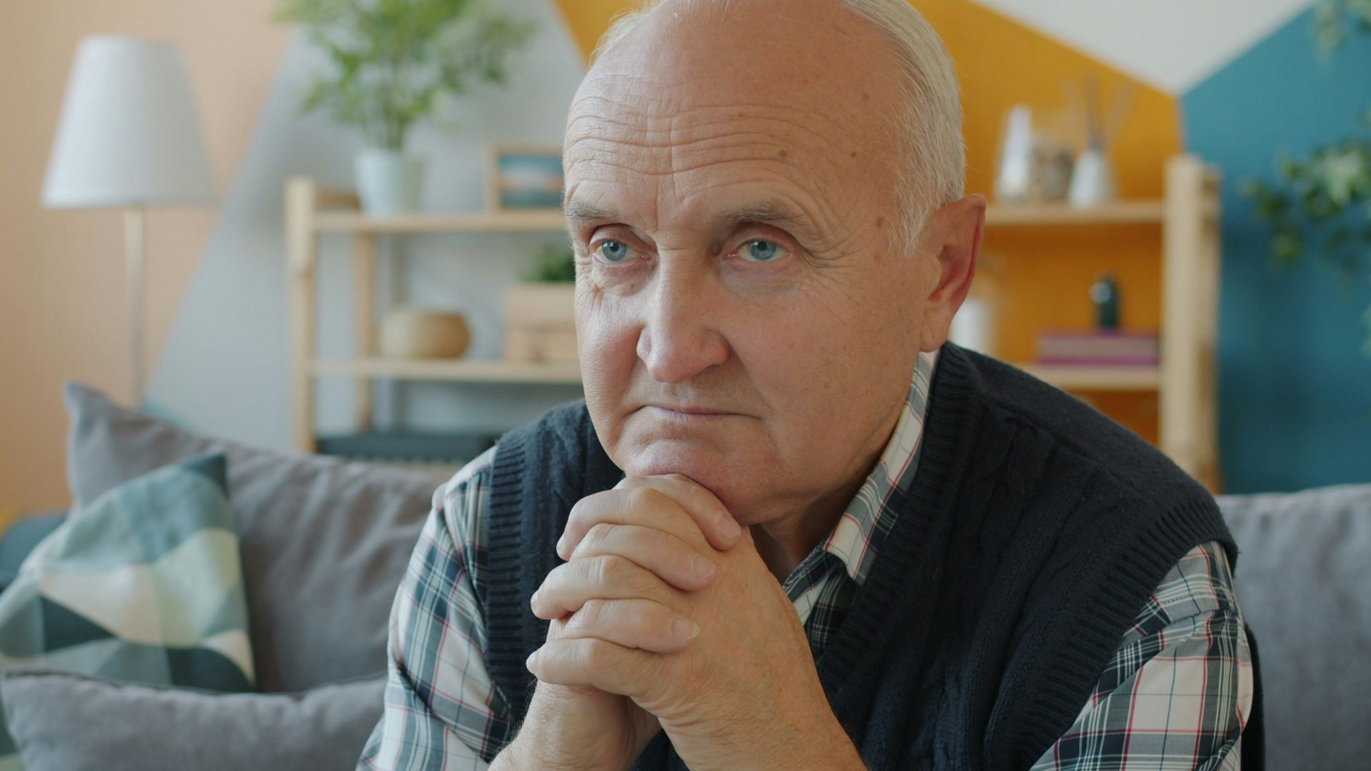 Elderly man sitting on a couch with hands clasped.