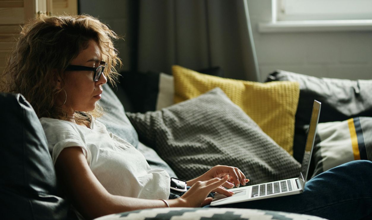 Young woman working on laptop while relaxing on a sofa with pillows, indoors