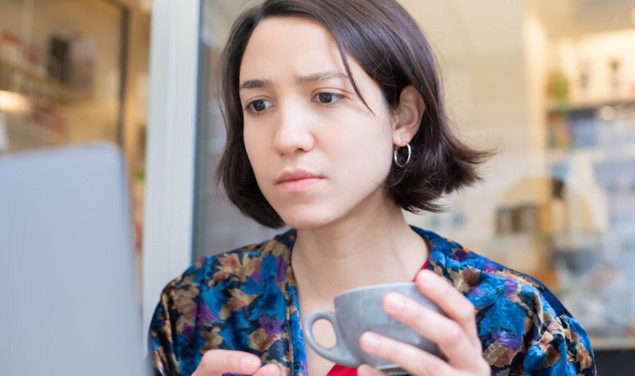 A woman attentively engages with her laptop while holding a cup of coffee, indoors