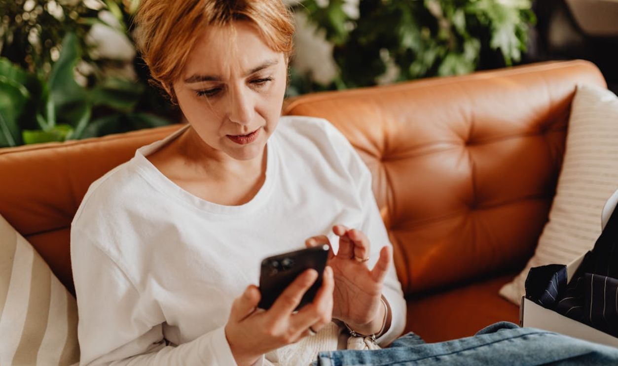Woman in casual attire using a smartphone on a cozy sofa surrounded by plants
