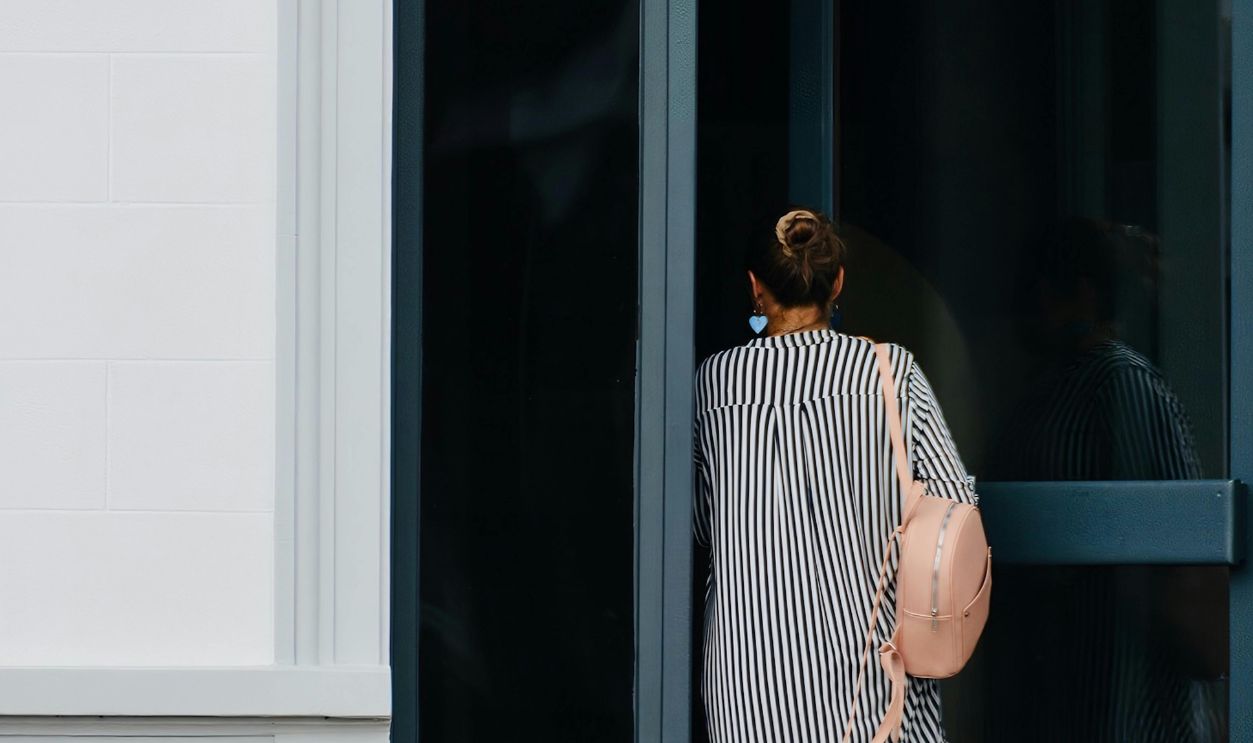 A woman entering a building through a modern glass doorway wearing a striped dress.