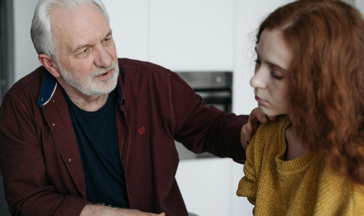 An elderly man consoles a young woman indoors, expressing empathy and understanding