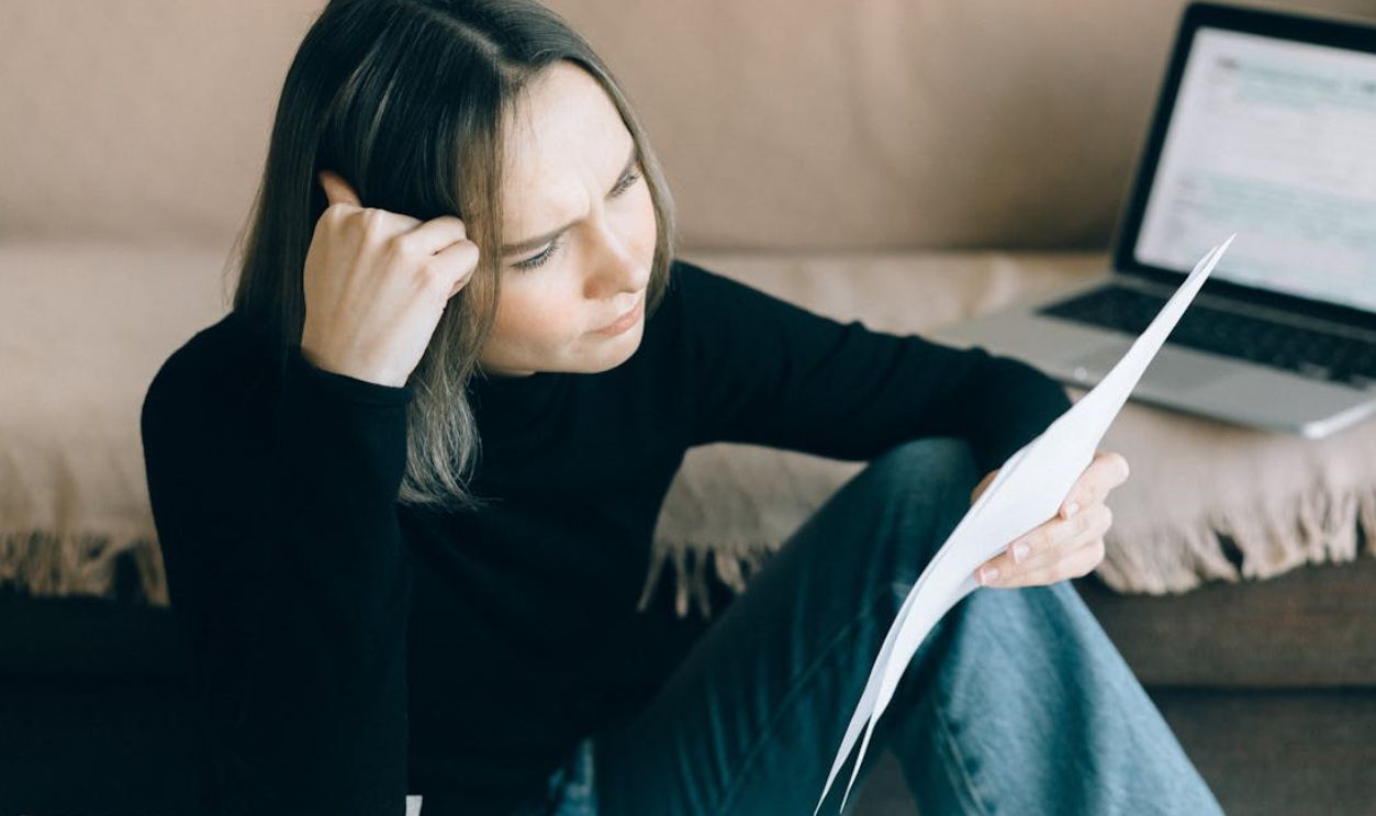 Focused woman analyzing papers with a laptop open, symbolizing thoughtful consideration