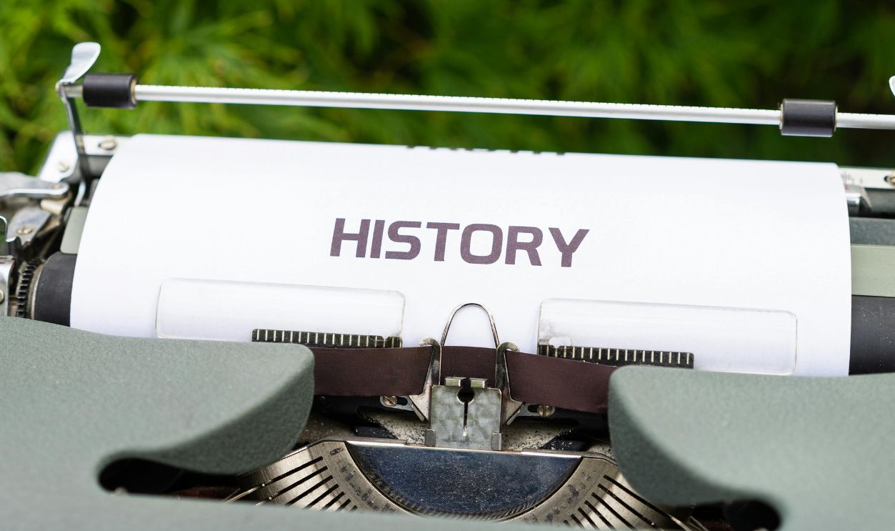 Close-up of a vintage typewriter with a paper labeled 'History' in an outdoor setting.
