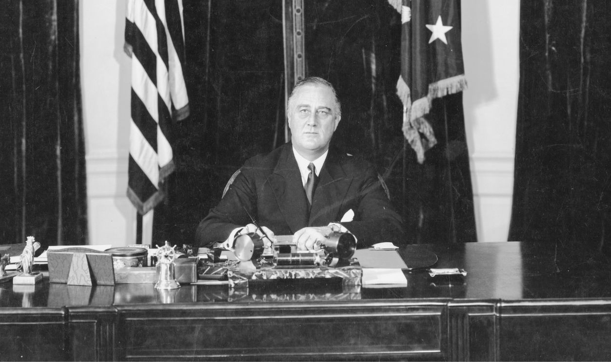 American President Franklin Delano Roosevelt (1882 - 1945) seated at his desk in front of American flags, circa 1940.