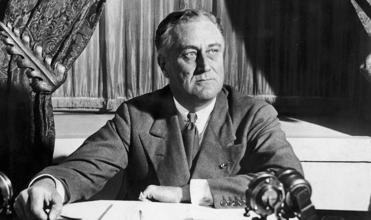  American President Franklin Roosevelt (1882 - 1945) sits at a desk with microphones, probably during a radio broadcast.