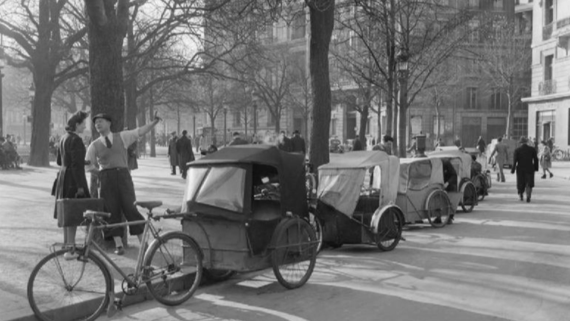 Parisian Traffic, Spring 1945- Everyday Life in Paris, France, 1945
A general view of a cab rank: French style!  A row of Velo taxis line the kerb of a leafy street in the Spring sunshine, somewhere in Paris.  Pedestrians can be clearly seen, going about 