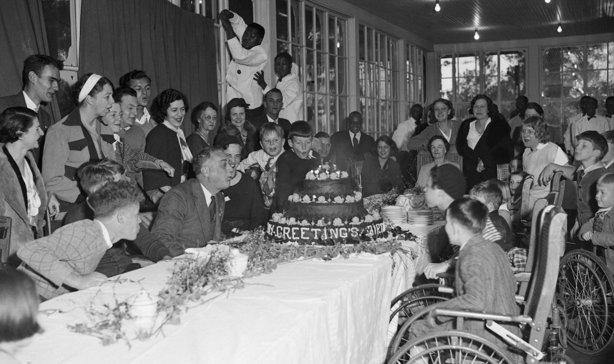 President-Elect Celebrates Birthday. Warm Springs, Georgia: Assisted by patients of the Warm Springs Foundation, President-Elect Franklin D. Roosevelt blows out the candles on his birthday cake during the celebration of his 51st anniversary at Warm Springs, Georgia. Mrs.Roosevelt is standing in rear wearing white headband.