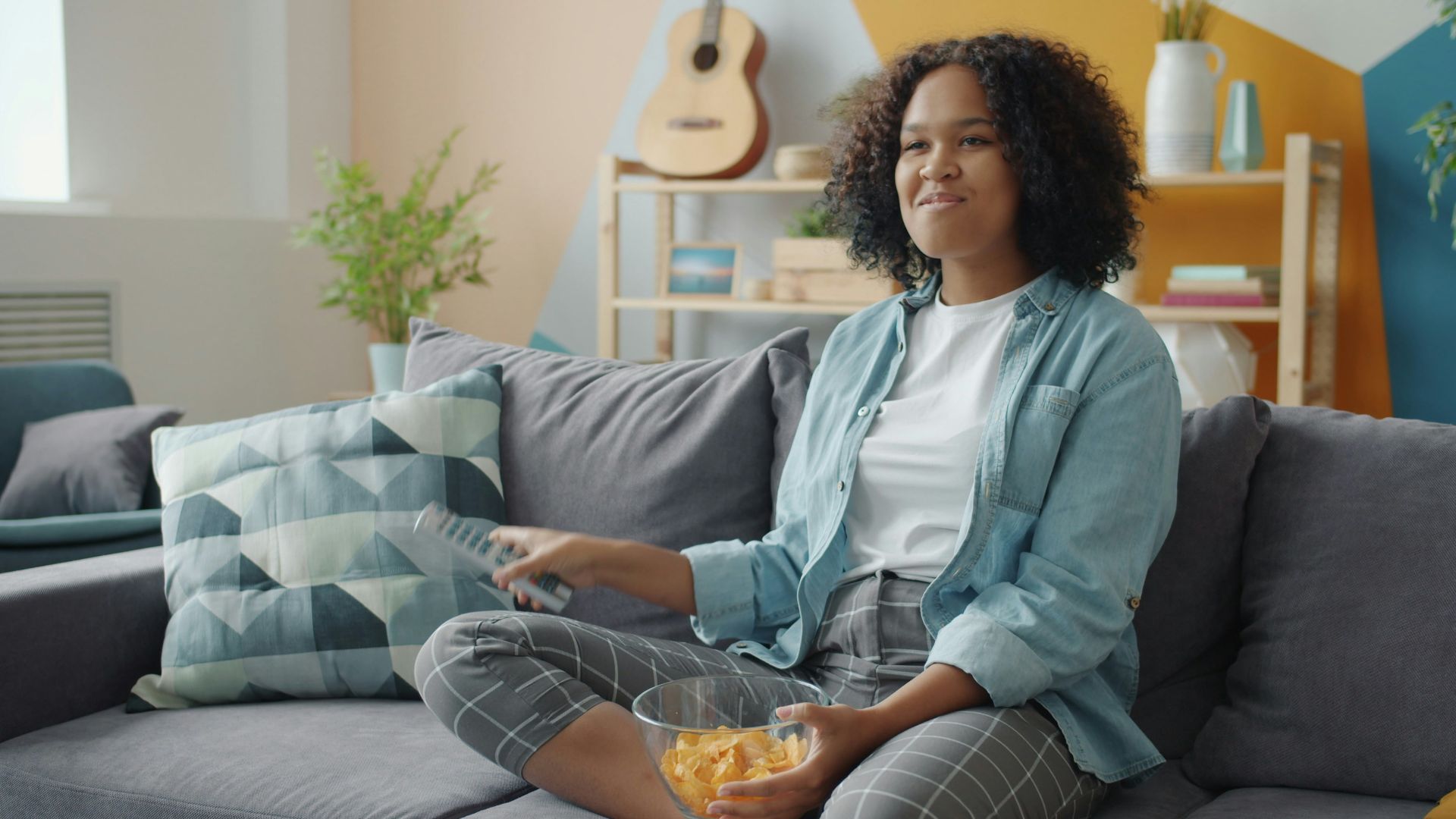 Young woman watching TV and eating snacks on couch.