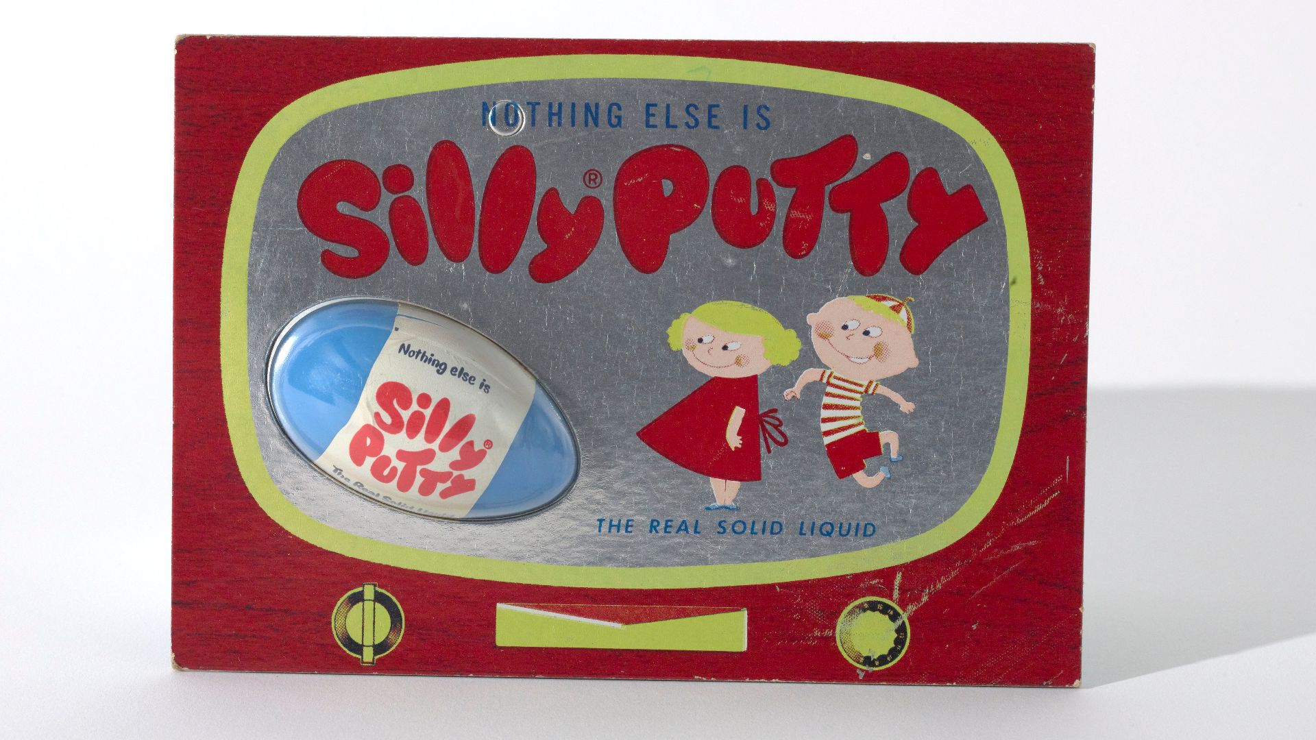 A rectangular cardboard package with a stylized television design and two illustrated cartoon children on the front. The cardboard package holds a blue plastic egg containing the Silly Putty. The back of the package describes various uses with illustratio